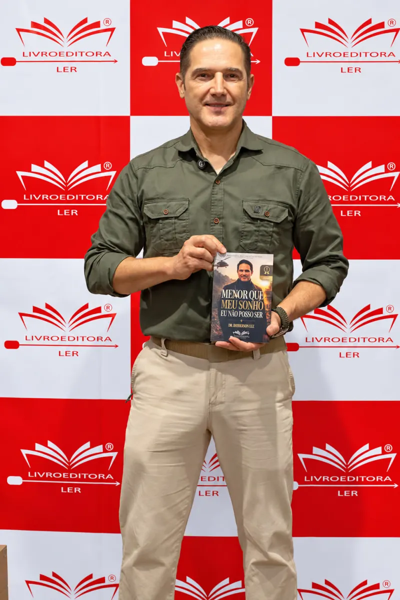Dr. Hemerson Luz posa com seu livro Menor que meu sonho, eu não posso ser no painel da Livro Editora